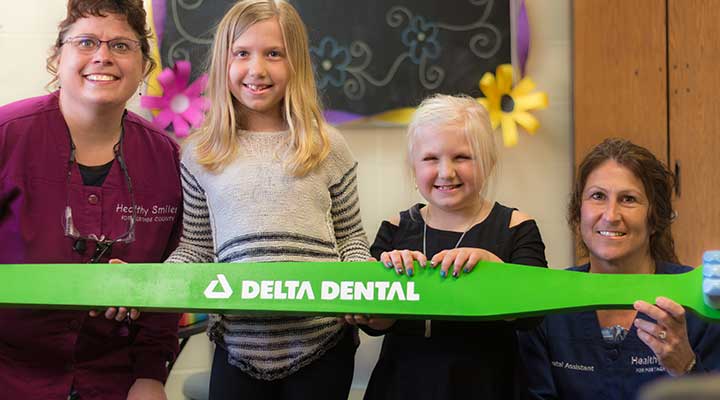Two hygienists hold a large, green Delta Dental toothbrush with two school-aged girls