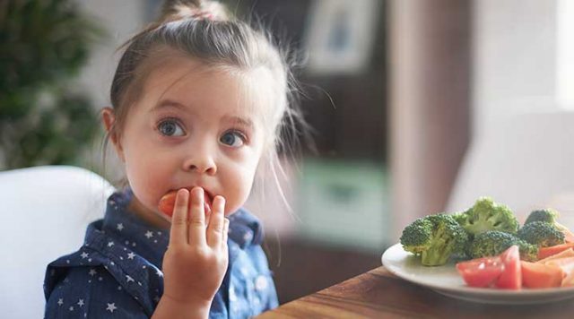 Young girl eating a tomato from a plate of vegetables