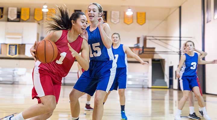 Girl playing basketball dribbles past her opponent