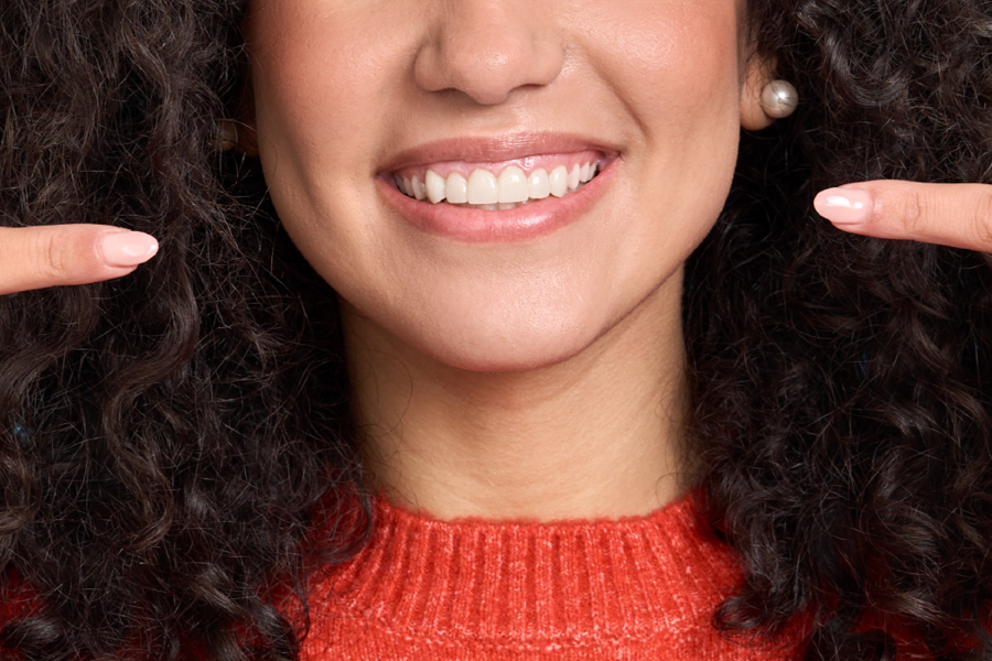 A woman in a red sweater points toward the veneers in her smiling mouth with both index fingers.